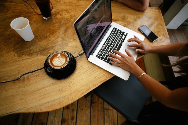 Person mit Kaffee und Laptop an einem braunen Holztisch